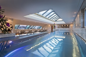 Una piscina interior moderna con tragaluces, sillones de descanso y vistas a la ciudad.
