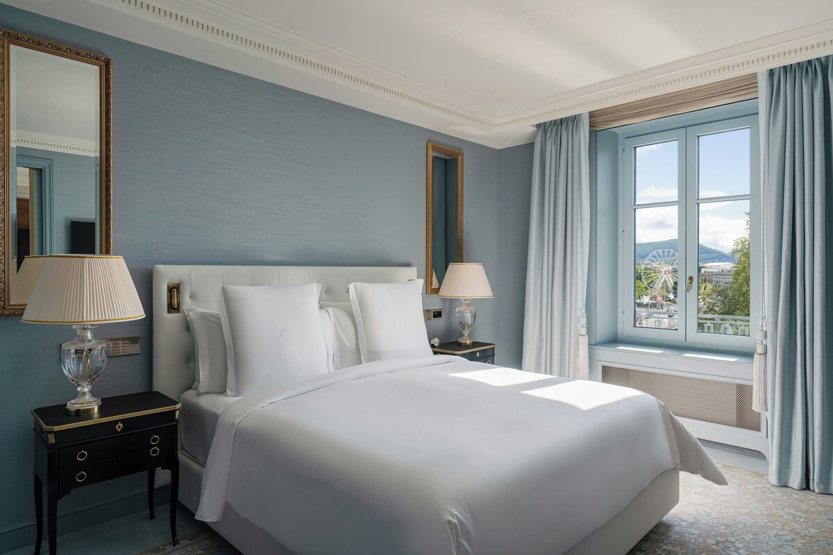 A hotel room with a large bed, two nightstands, a window with curtains, and a view of a Ferris wheel.