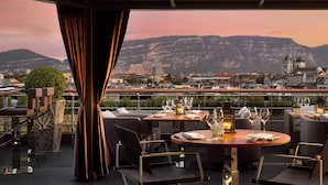 Un espace extérieur aménagé pour les repas, avec des tables et des chaises, offrant une vue sur le paysage urbain et les montagnes.