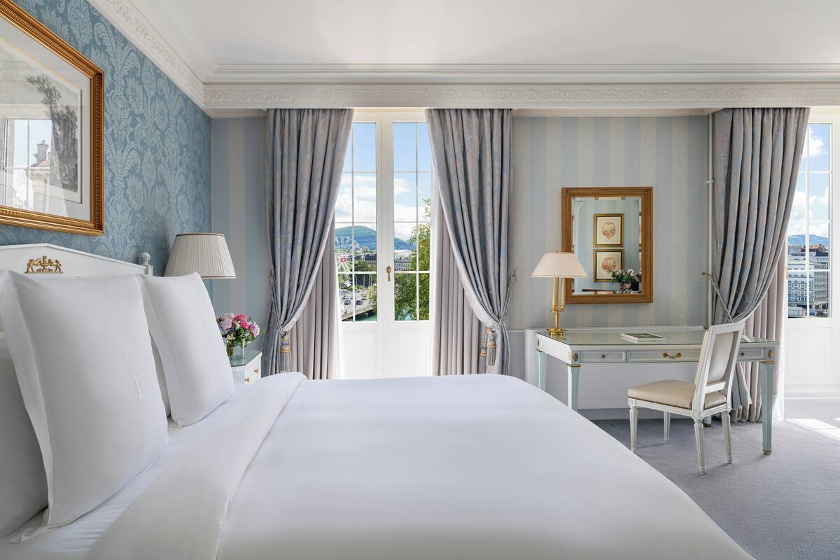 Une chambre d’hôtel avec un grand lit, un bureau avec une chaise, un miroir et une vue sur le paysage urbain par la fenêtre.
