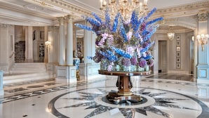 Un vaste hall d’entrée avec un sol en marbre, un grand arrangement floral et des lustres richement décorés.