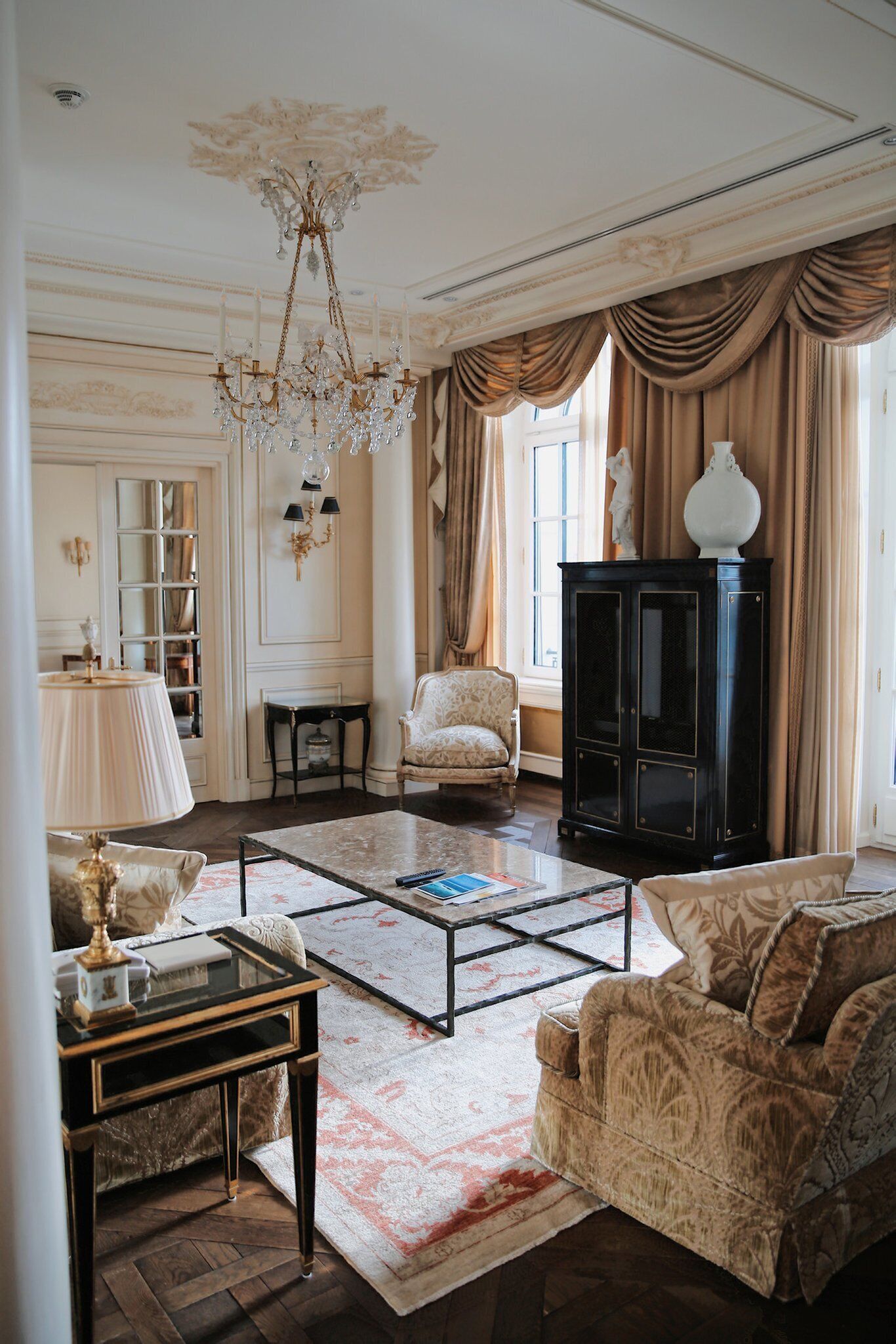 Una sala de estar clásica con una araña, un mueble negro y una alfombra estampada.