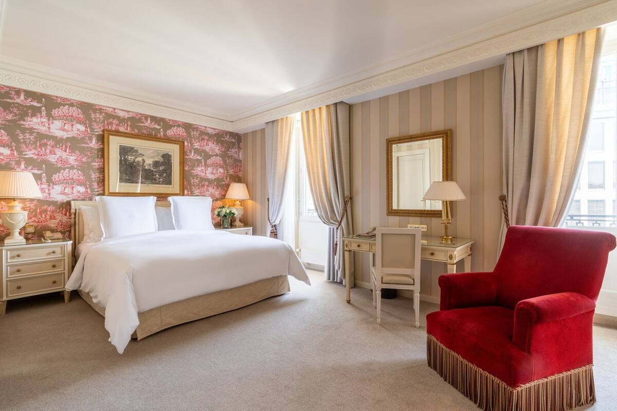 Une chambre d’hôtel avec un grand lit, un bureau, une chaise et une fenêtre avec des rideaux.