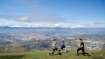 Three people jogging on a grassy hill with a cityscape and mountains in the background.