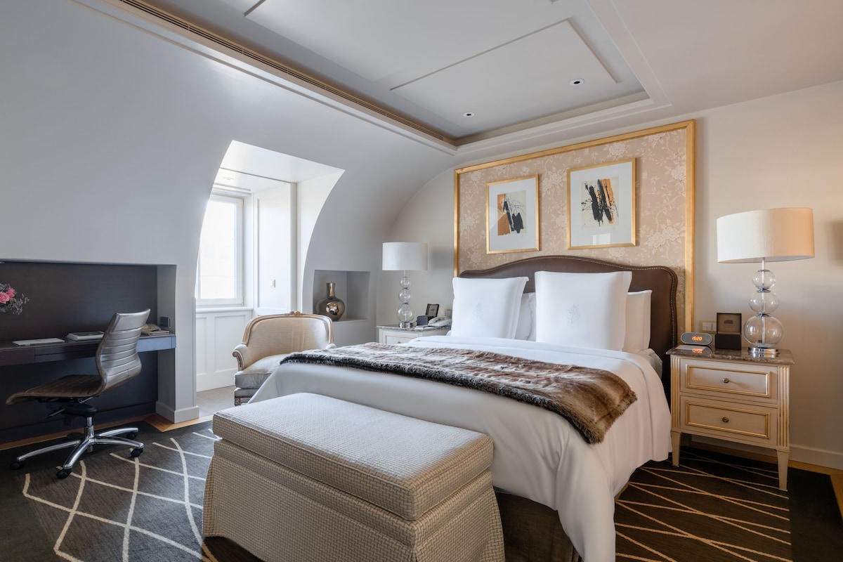 Habitación de hotel con una cama grande, un escritorio, una silla, una lámpara y obras de arte en la pared.