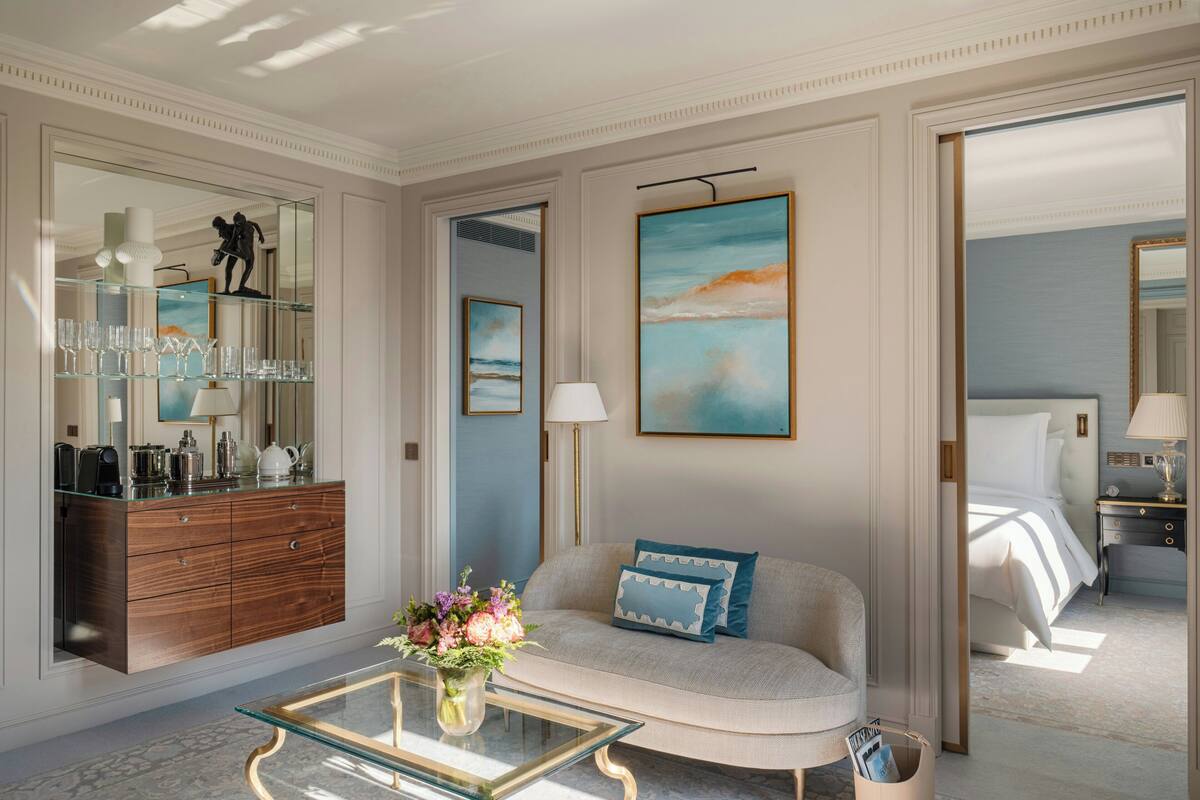 Une chambre d’hôtel moderne, dotée d’un canapé, d’une table basse en verre ornée de fleurs, d’une commode et d’un grand tableau accroché au mur.