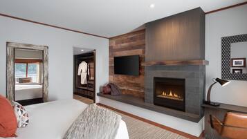 A modern hotel room with a large bed, a fireplace, a mounted TV, and a view of the outdoors.