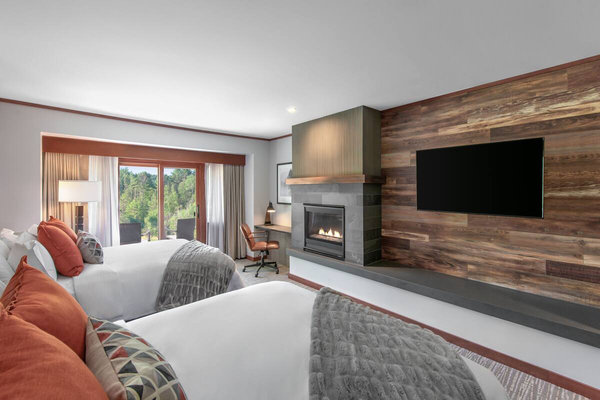 A modern hotel room with a fireplace, a flat-screen TV, and a large window offering a view of the outdoors.