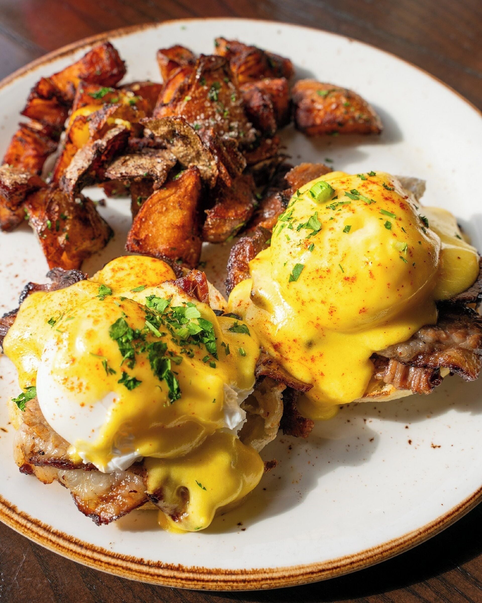 A plate of eggs benedict with poached eggs, hollandaise sauce, and fried potatoes.