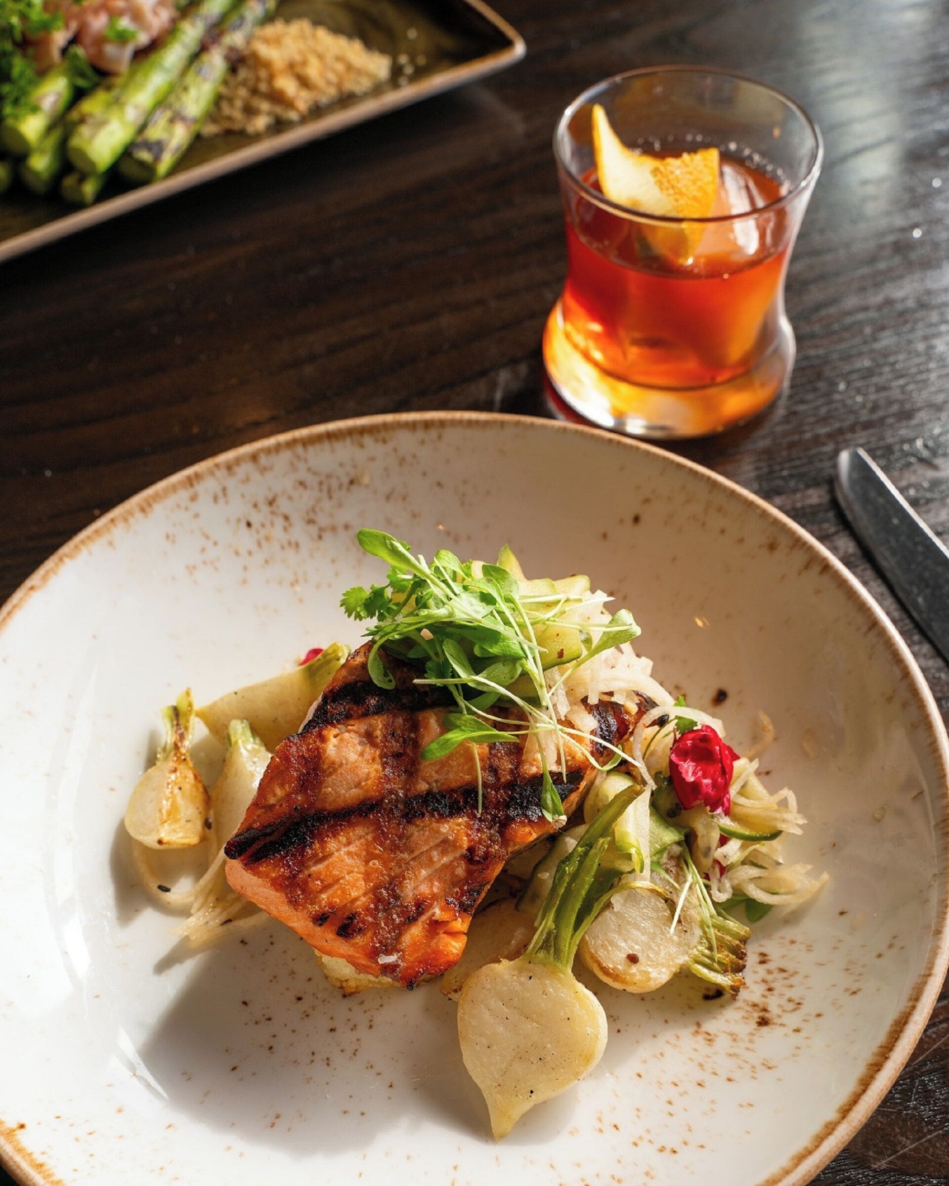 A plate of grilled salmon with vegetables and a glass of red beverage on a wooden table.