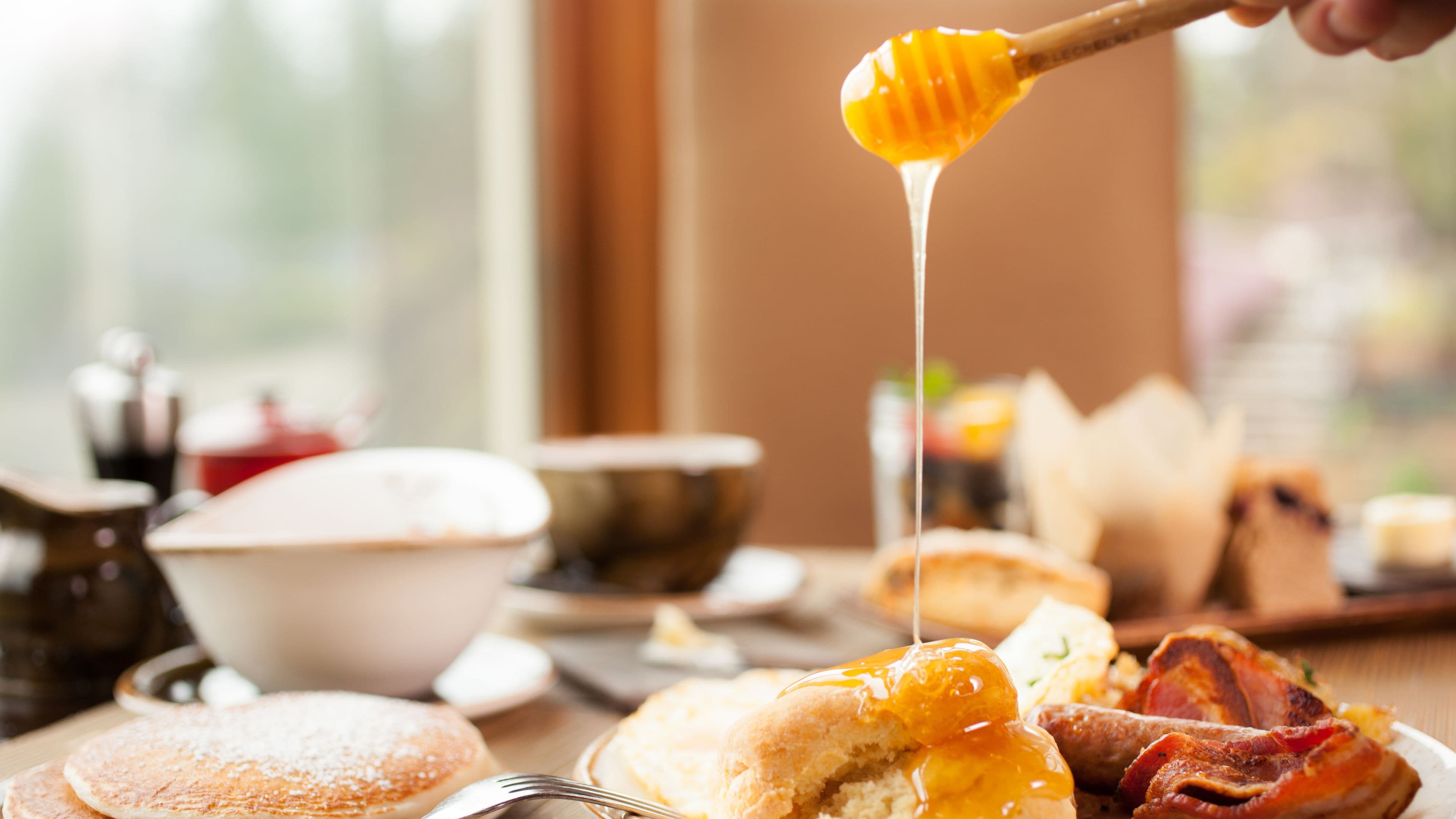 Une table de petit-déjeuner avec des crêpes, du bacon et un récipient à miel.