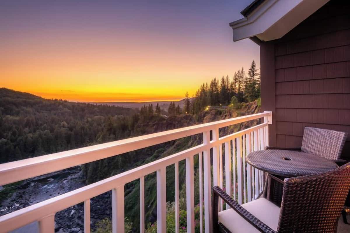 A balcony with a view of a forest and a river at sunset.