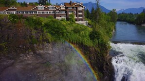 A hotel with multiple floors, a river in the background, and a waterfall with a rainbow. - Salish Lodge & Spa (Fall City)
