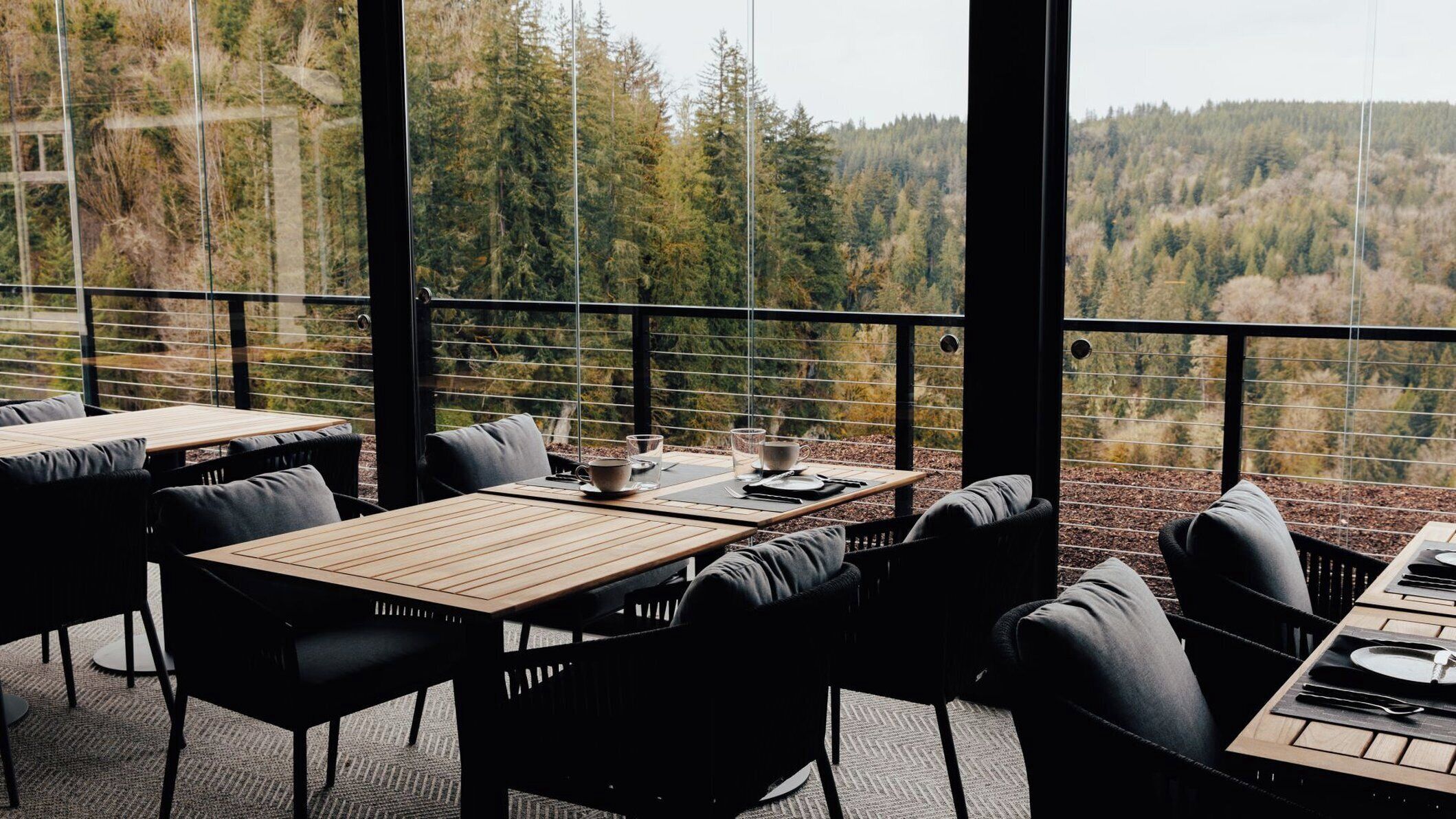 An outdoor dining area with tables and chairs, overlooking a forested landscape.