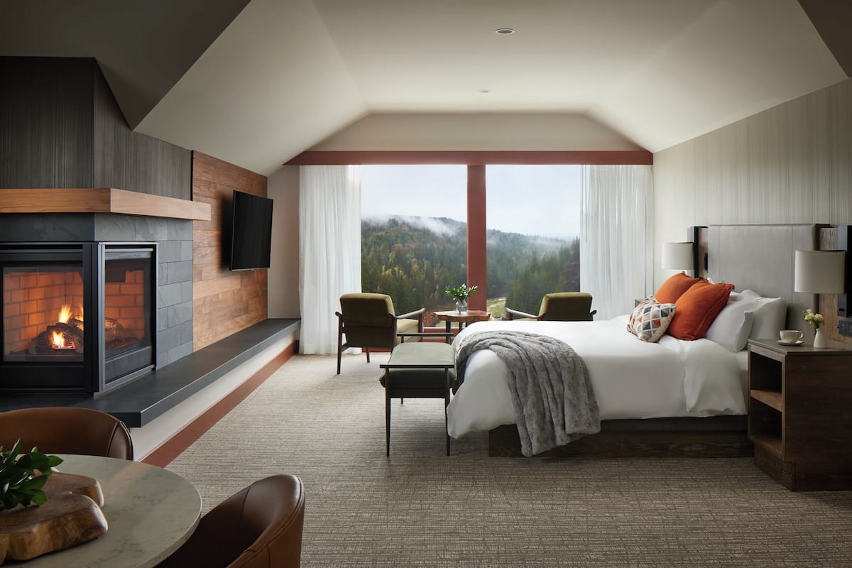 A hotel room with a fireplace, a bed, a desk, and a view of the outdoors.