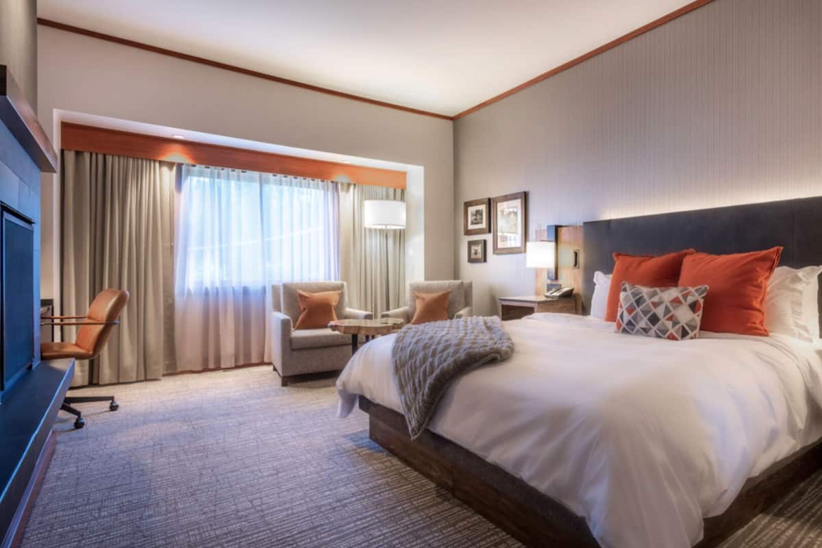 A hotel room with a large bed, two armchairs, a desk, and a TV.