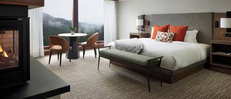 A hotel room with a bed, a bench, a fireplace, a round table, and a view of the mountains.