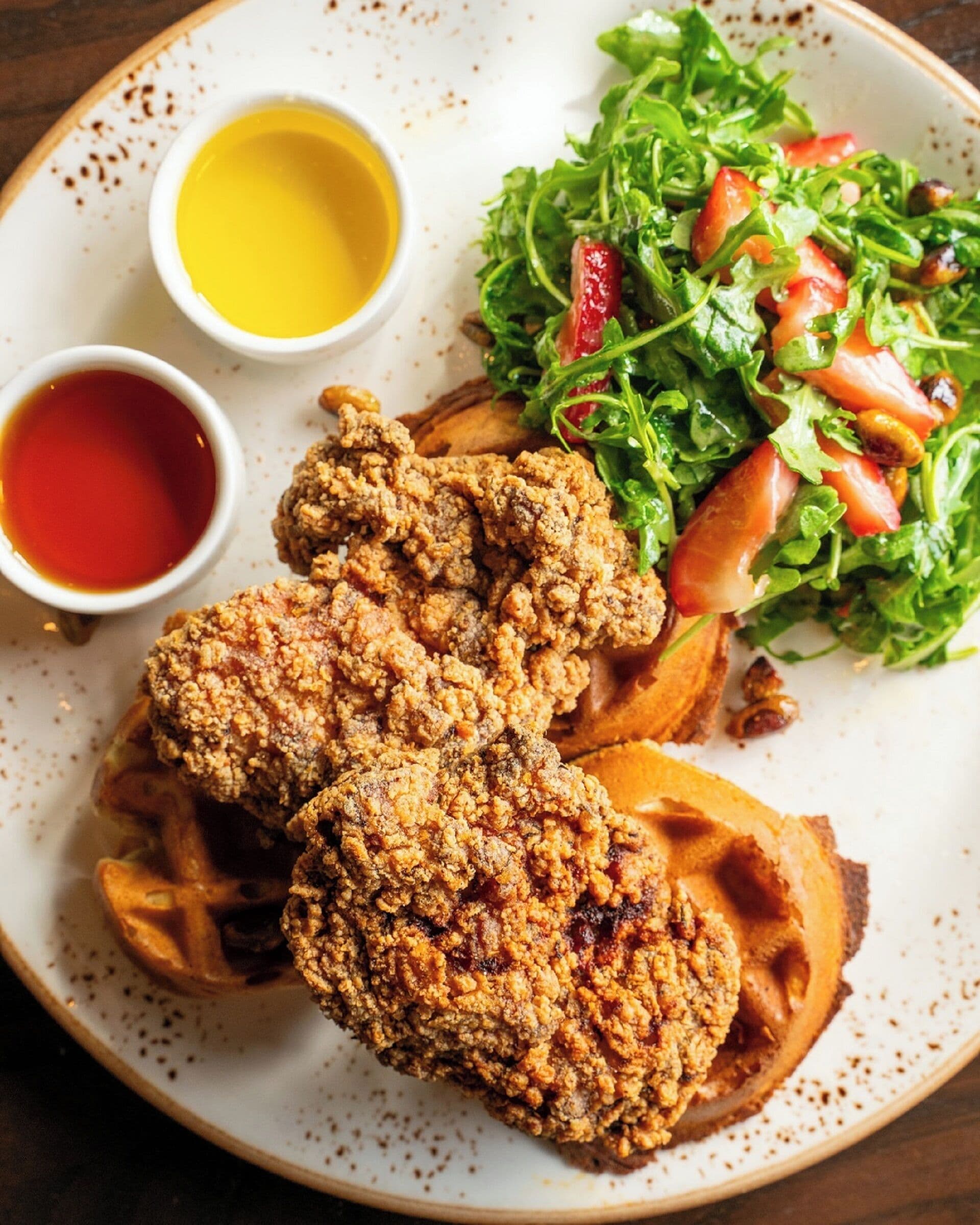 Un plato con pollo frito, gofres y una ensalada con fresas.