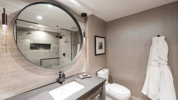 A modern bathroom with a large round mirror, a white sink, a toilet, and a robe hanging on the wall.