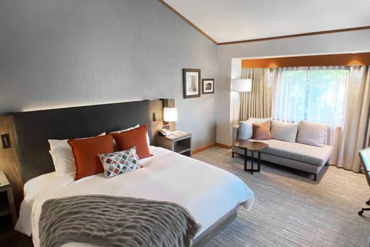 A hotel room with a large bed, a sofa, a small table, and a nightstand.