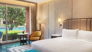 A hotel room with a large bed, a chair, a small table, and a view of the outdoors.