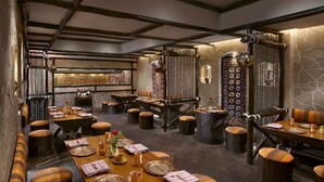 A restaurant with high wooden beams, stone walls, and multiple dining tables with stools.
