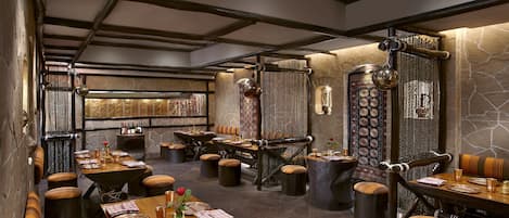 A restaurant with high wooden beams, stone walls, and multiple dining tables with stools.
