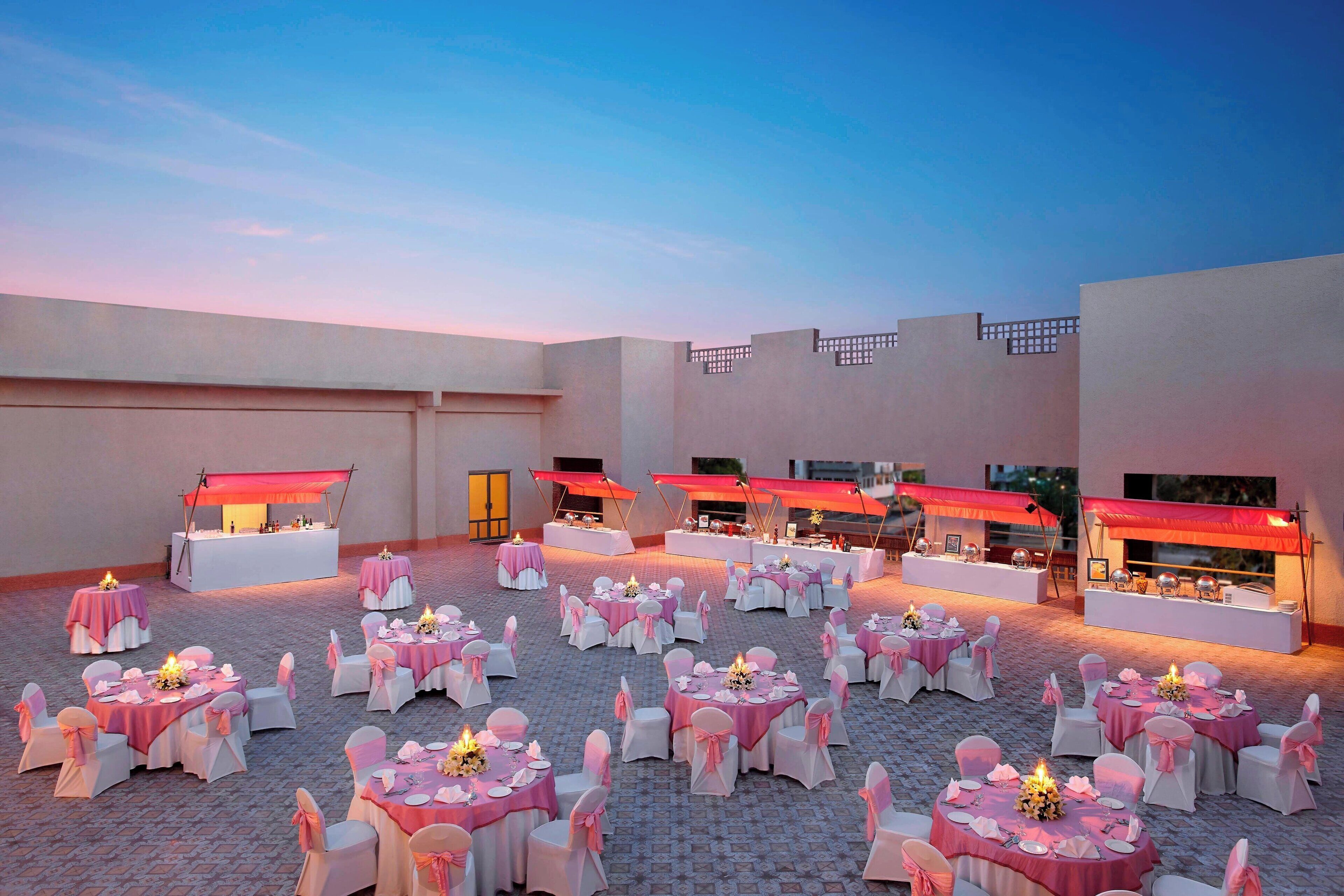 Un espacio para eventos al aire libre con mesas y sillas redondas, cubierto por toldos rojos y un piso de ladrillo.