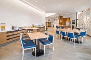 Un comedor moderno con mesas de madera y sillas con cojines azules, una encimera de cocina con utensilios y una pared decorativa con círculos.