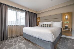 A hotel room with a large bed, a nightstand with a clock, and a window with curtains.