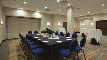 A conference room with a long table, blue chairs, and white tables with tablecloths.