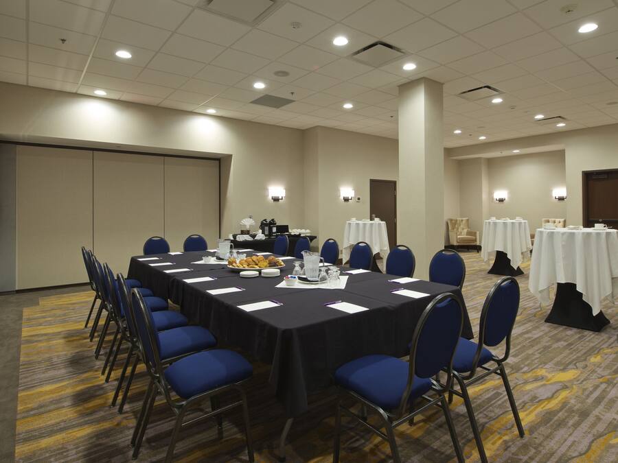 A conference room with a long table, blue chairs, and white tables with tablecloths.