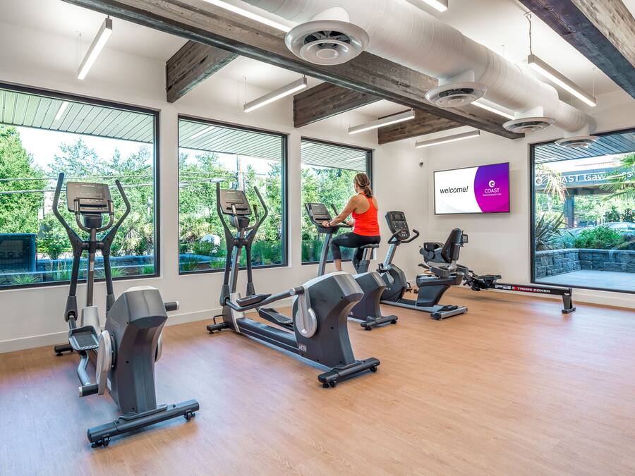 Un gimnasio con máquinas de cardio, ventanas amplias y un cartel motivacional.