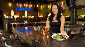 A bar area with a neon sign, bar stools, and a person holding a drink.