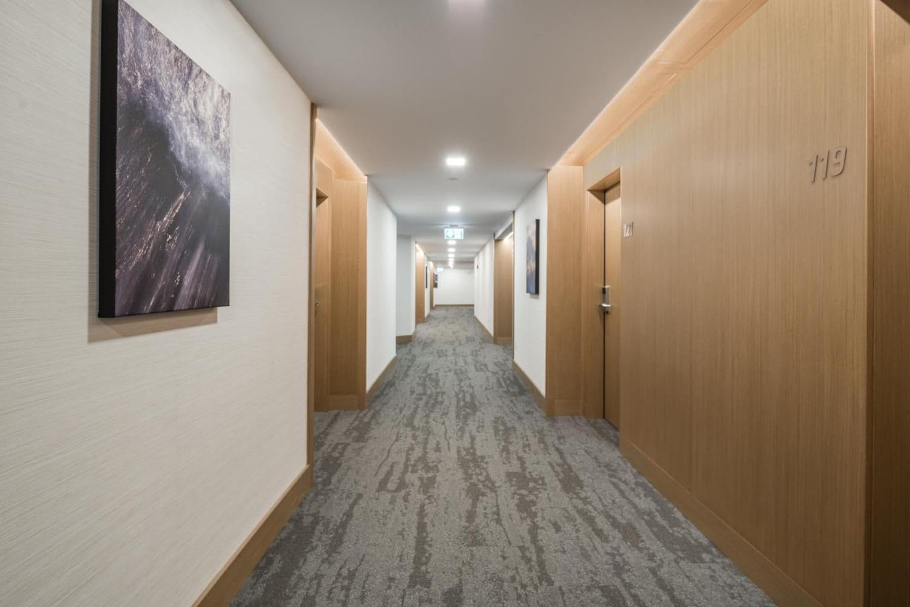 A hotel hallway with carpeted floors, wooden doors, and a framed picture on the wall.