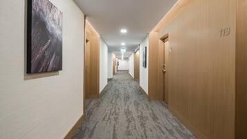 A hotel hallway with carpeted floors, wooden doors, and a framed picture on the wall.
