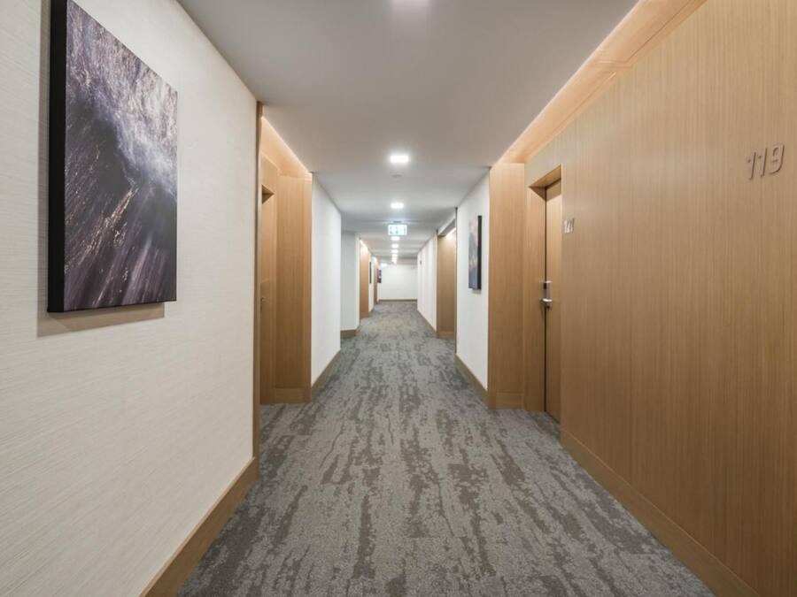 A hotel hallway with carpeted floors, wooden doors, and a framed picture on the wall.