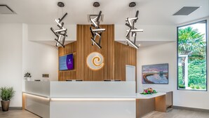 A modern reception desk with a wooden panel backdrop, a digital screen, and a large window offering a view of greenery. - Coast Tsawwassen Inn (Delta)