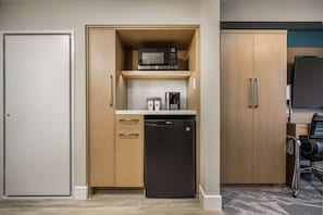 Compact kitchenette with microwave, coffee maker, and dishwasher, surrounded by cabinetry and a door.