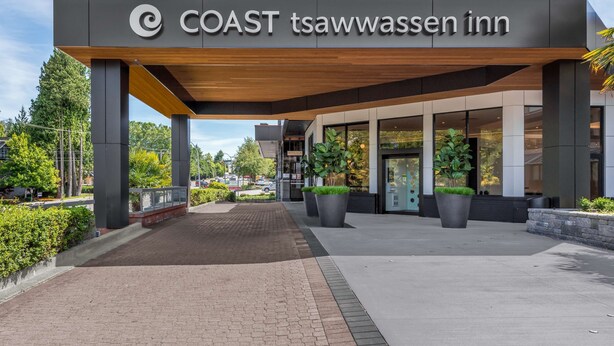 The exterior of the COAST tsawwassen inn with a modern design, featuring a covered entrance, large windows, and potted plants. - Coast Tsawwassen Inn (Delta)