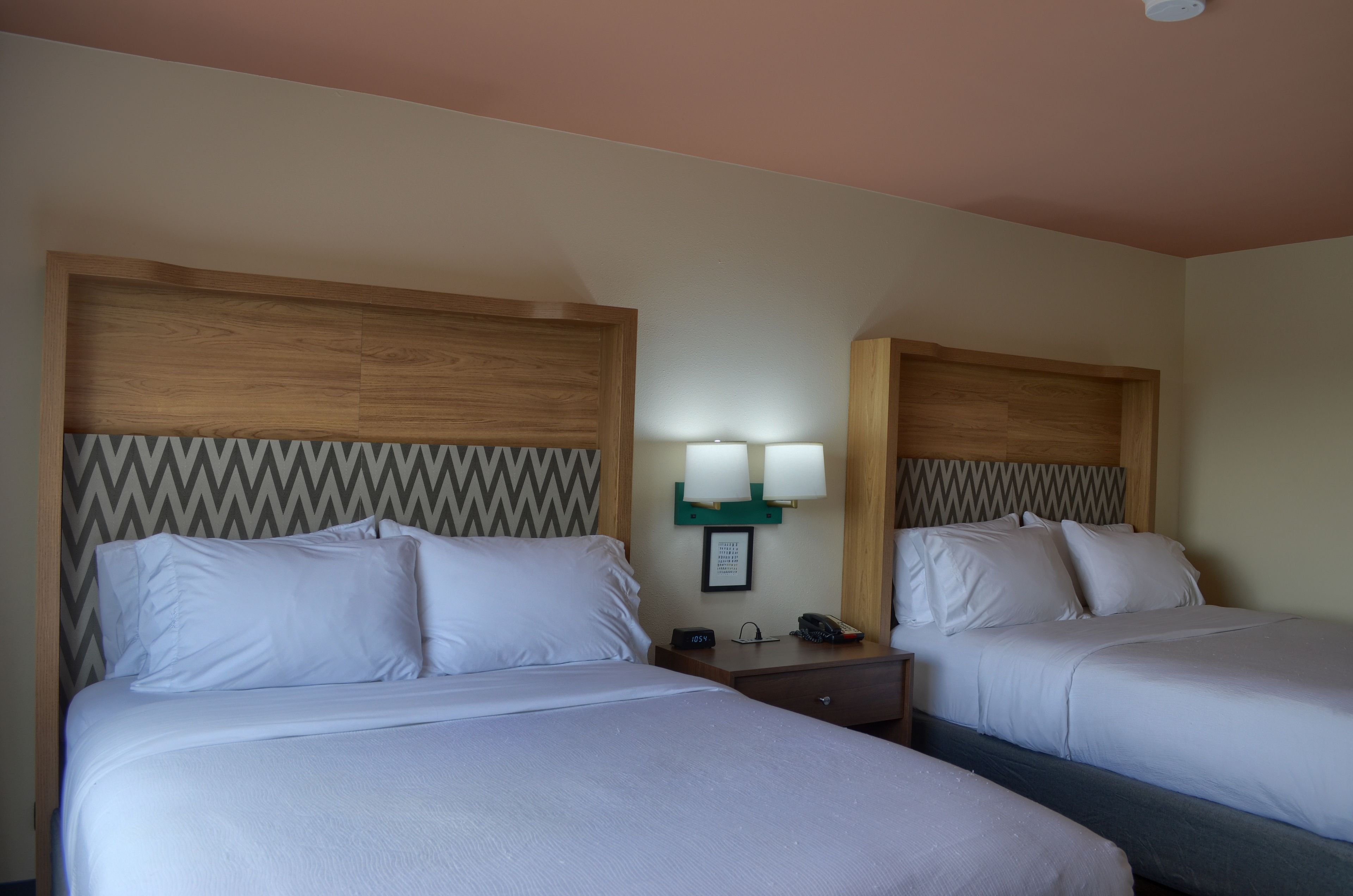 A hotel room with two beds, wooden headboards, a nightstand with a lamp, and a framed picture on the wall.
