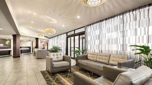 Eine moderne Lobby mit einer Rezeption, einer Sitzecke mit Sofas und Sesseln, dekorativer Beleuchtung und einem gemusterten Boden.