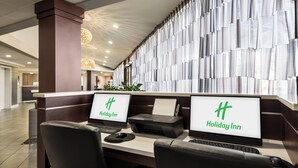 Ein Hotelrezeptionstresen mit zwei Monitoren, die das Holiday Inn Logo zeigen, einem Drucker und einem Computer.