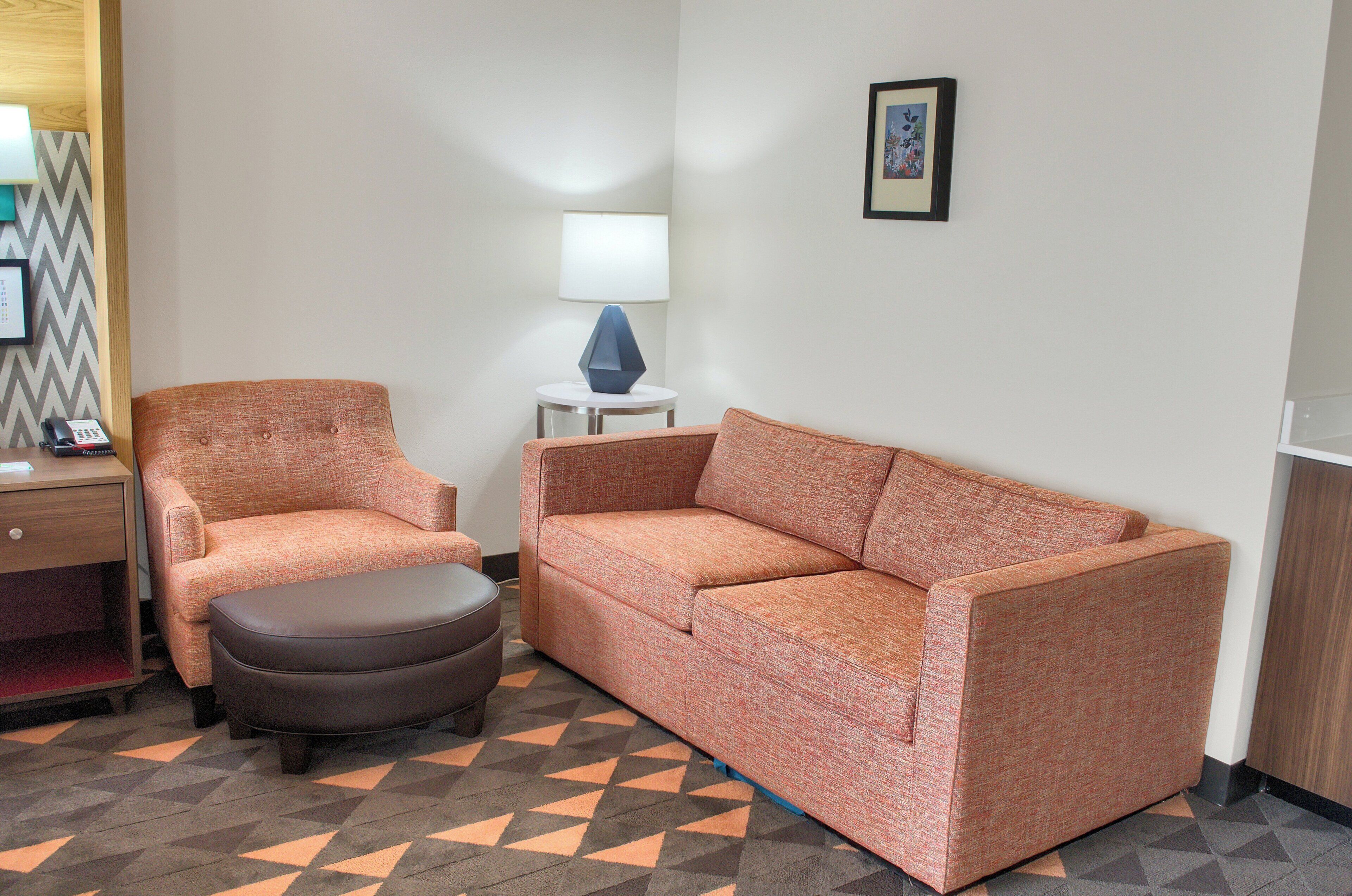A room with a sofa, an ottoman, a lamp, a small table, and a chair.