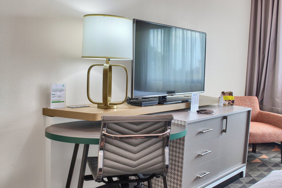 A hotel room with a desk, a television, a chair, and a cabinet.