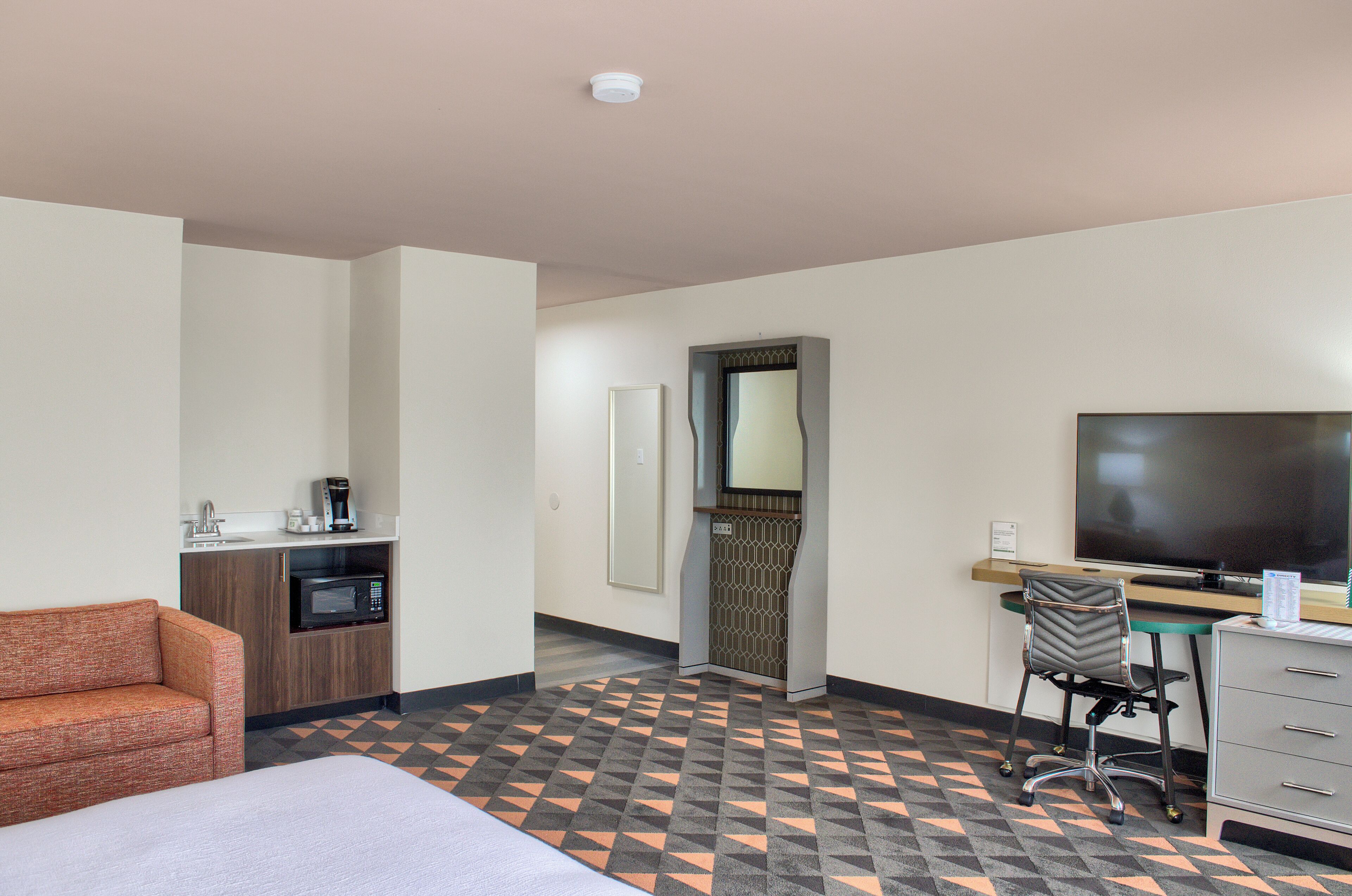 A hotel room with a sofa, a desk with a computer, a flat-screen TV, a microwave, and a coffee maker.