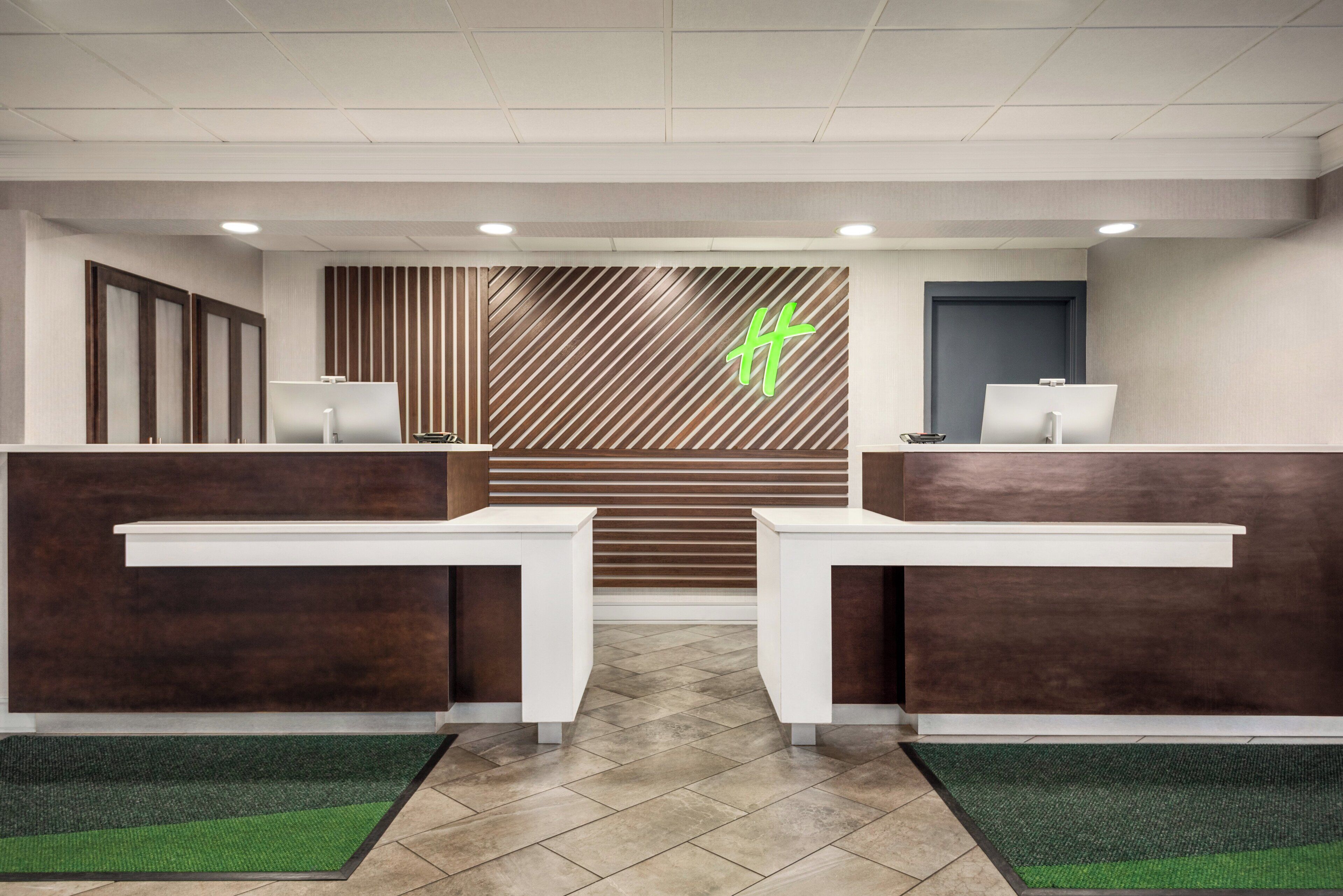 Un espace d’accueil comprenant deux comptoirs de réception, un mur à lambris en bois et un logo vert.