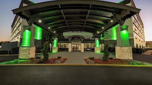Ein moderner Hotel Eingangsbereich mit gewölbter Dachkonstruktion, grün beleuchteten Säulen und angelegter Grünfläche.