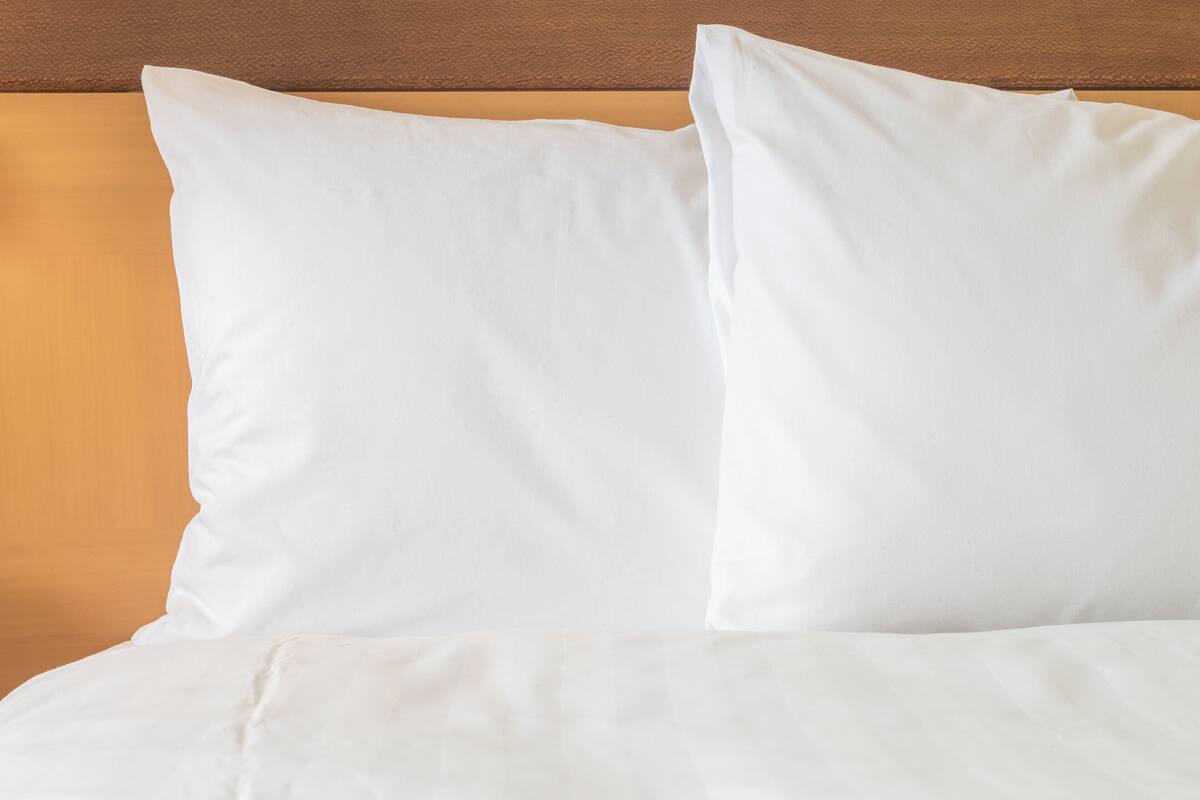 A bed with white bedding and pillows against a wooden headboard.