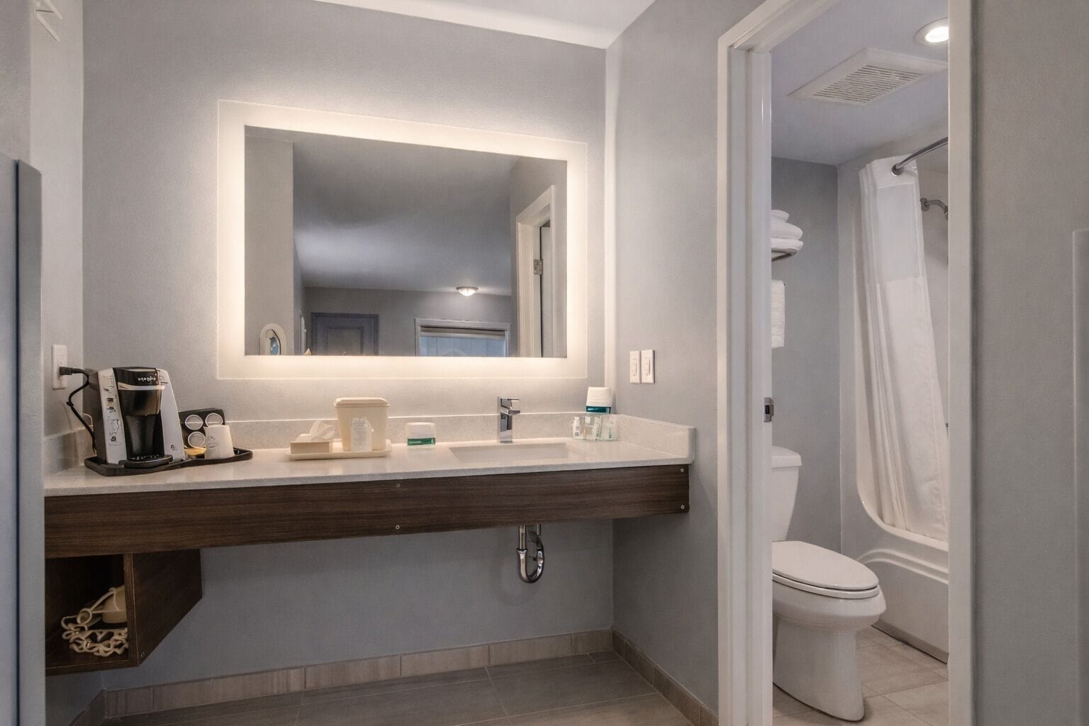 Un baño moderno con un espejo grande, una cafetera y un inodoro.